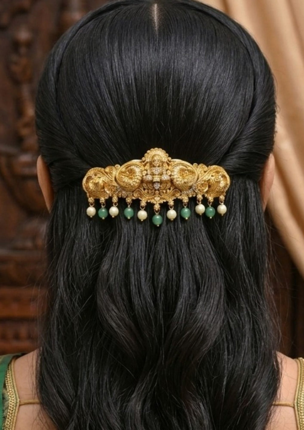 Decorative hair accessory with gold, green, and pearl elements Traditional Laxmi hair accessory gold plated design featuring a beautifully crafted Lakshmi Devi motif at the center surrounded by intricate peacock and floral carvings. The accessory is enhanced with sparkling zircon stone accents, elegant green bead drops and pearl hangings, creating a rich South Indian temple jewelry look perfect for bridal hairstyles, weddings, festivals and classical dance performances.