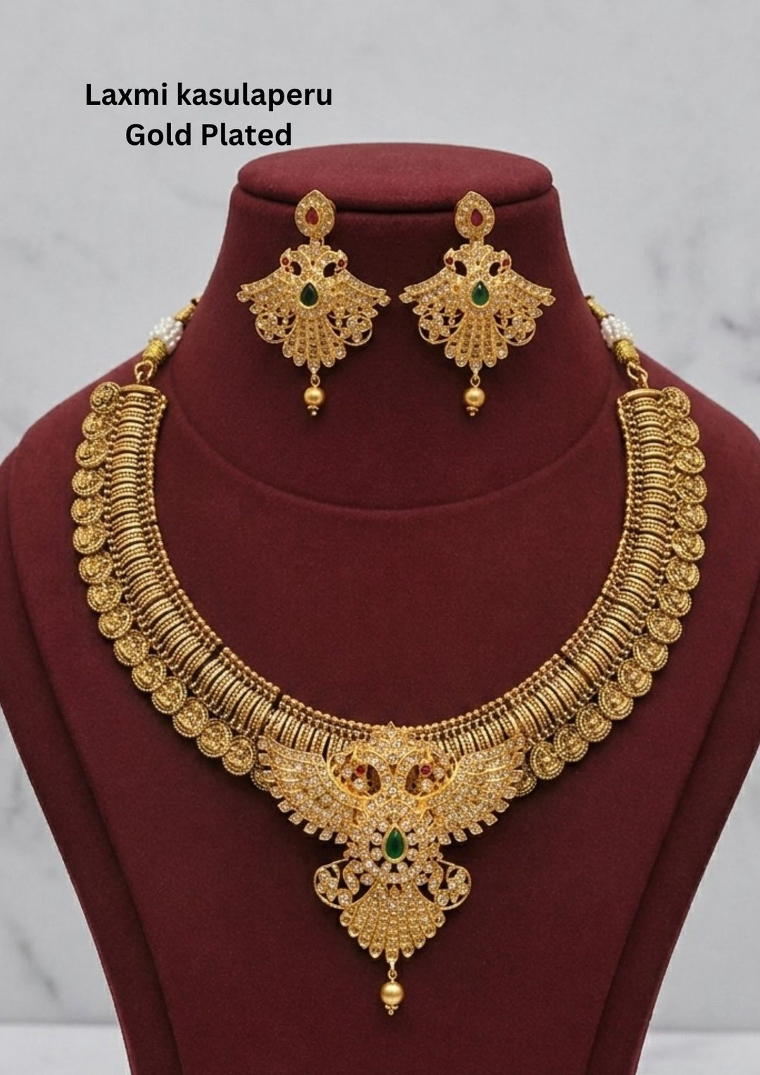 Traditional Laxmi kasulaperu gold plated short haram necklace featuring detailed coin style motifs throughout the chain with an intricately designed center pendant studded with white stones and green stone accents. The matching earrings have elegant filigree detailing with hanging gold beads, creating a rich South Indian temple jewelry appearance suitable for weddings, poojas and bridal occasions.