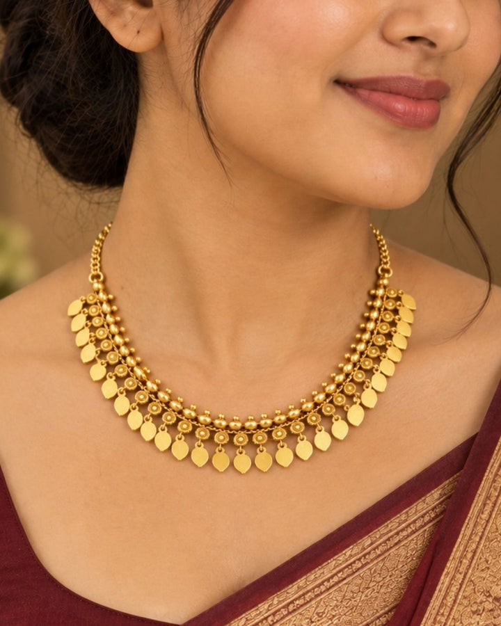 Elegant gold plated traditional necklace featuring multiple leaf-shaped charms, circular textured motifs, and beaded detailing, perfect for festive and traditional wear.