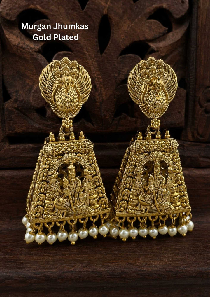 Gold-plated Murgan jhumkas gold plated temple earrings designed with peacock and lord murgan in sitting position, traditional South Indian style, hanging white pearl drops, suitable for weddings, temple functions, festivals, Bharatanatyam, sarees, lehengas, and ethnic festive wear with rich royal appearance.
