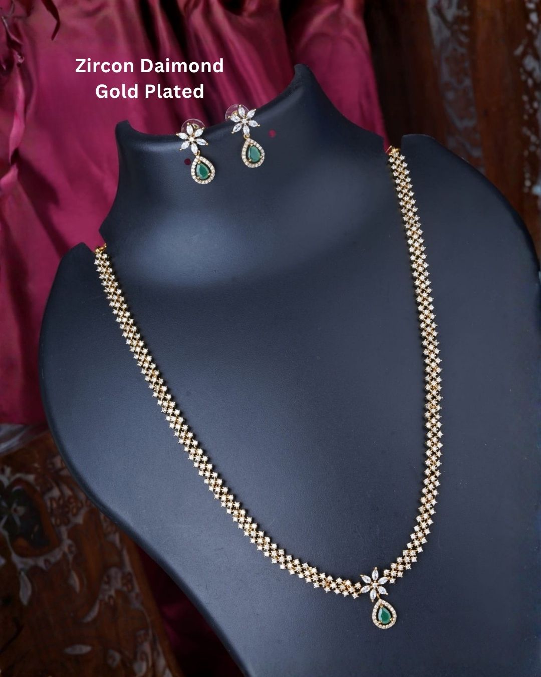 Gold plated zircon necklace and matching earrings displayed on a black jewellery bust against a rich burgundy background.