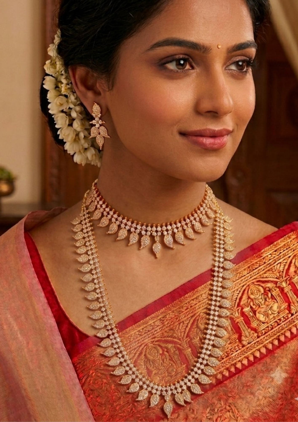 Woman wearing traditional jewelry Traditional Panchaloham gold plated bridal combo set featuring a short choker necklace and a matching long haram chain, both intricately designed with repeating mango leaf motifs densely studded with shimmering white stones. The collection is beautifully paired with matching delicate leaf drop earrings that complete the uniform elegant look and skin-friendly 