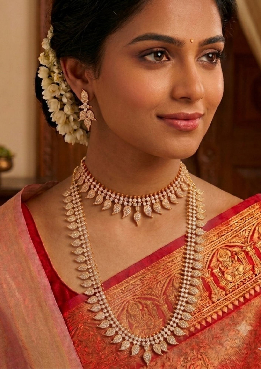Woman wearing traditional jewelry Traditional Panchaloham gold plated bridal combo set featuring a short choker necklace and a matching long haram chain, both intricately designed with repeating mango leaf motifs densely studded with shimmering white stones. The collection is beautifully paired with matching delicate leaf drop earrings that complete the uniform elegant look and skin-friendly 