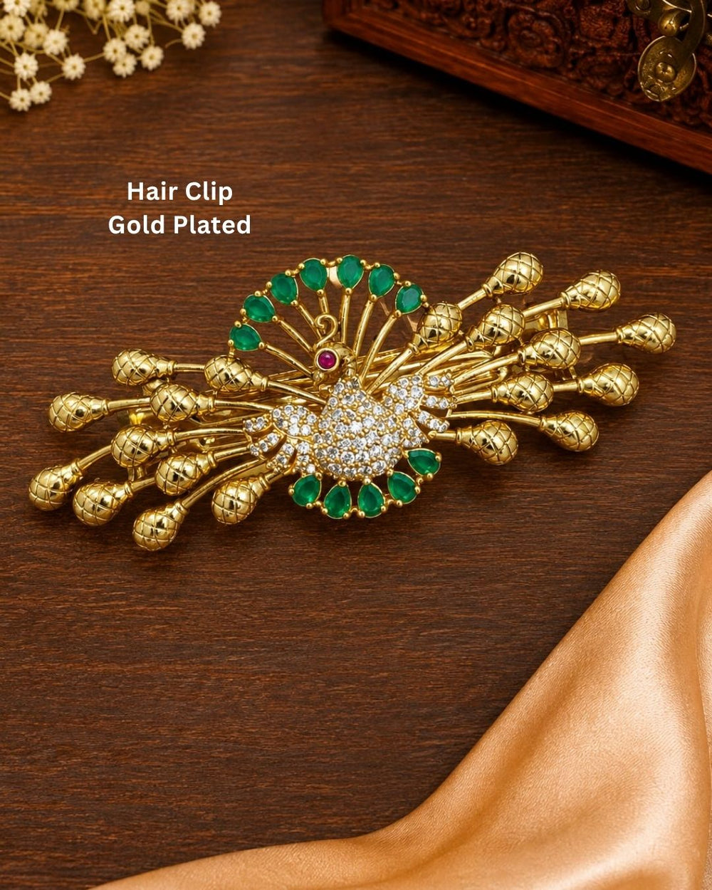Traditional gold plated designer hair clip featuring an ornate peacock motif surrounded by green stones and sparkling white stones, with multiple decorative gold bead accents, perfect for festive and traditional hairstyles.