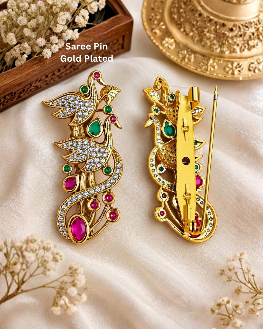 Pair of gold plated double peacock saree pins displayed on a light wooden surface, showcasing sparkling stones and decorative pin-back fastenings.