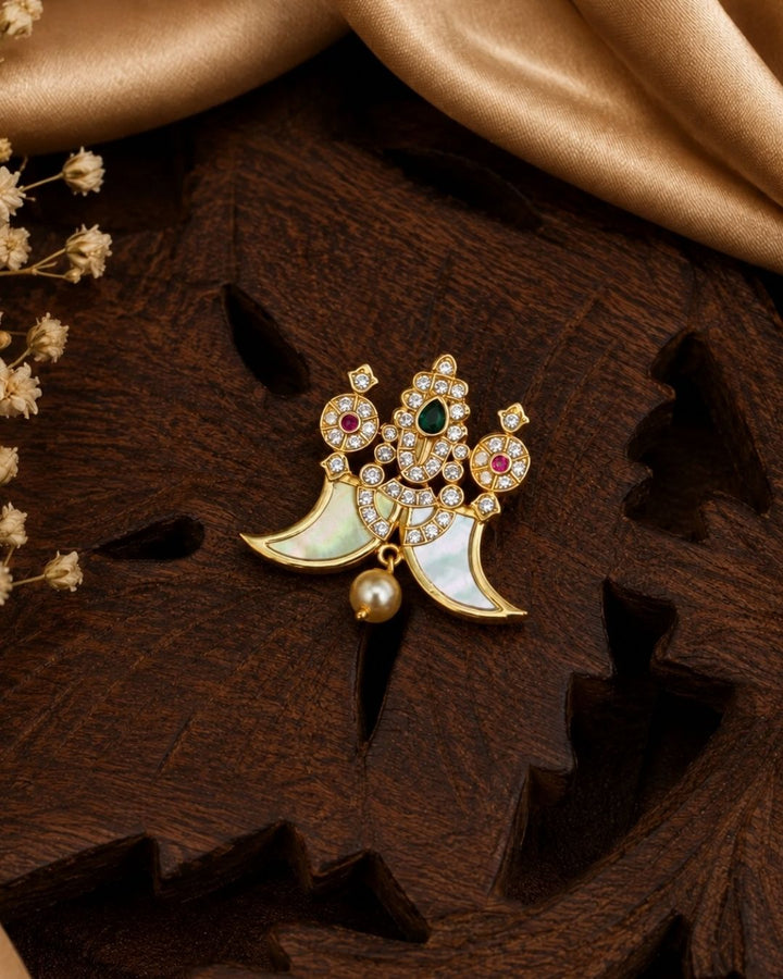 Shop this elegant gold plated peacock pendant featuring a green stone centerpiece, sparkling stones, mother-of-pearl accents, and a pearl drop. Perfect for festive and traditional occasions.