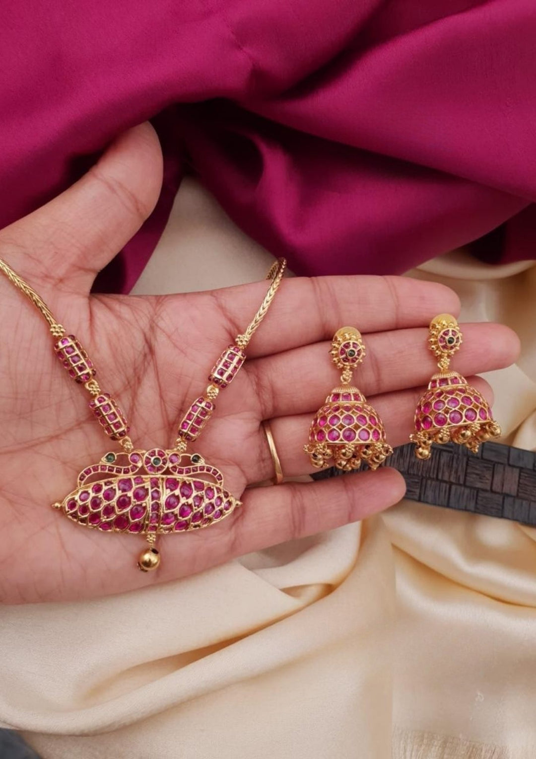 Premium gold plated ruby stone choker necklace set featuring an intricate central floral-inspired pendant and matching jhumka earrings embellished with ruby-colored stones. Perfect for weddings, festive occasions, traditional wear, parties, and gifting.