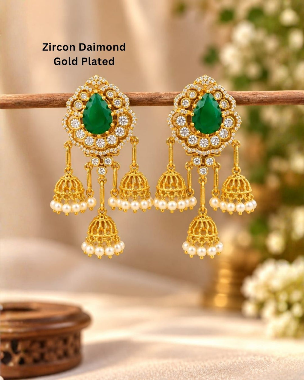 Gold plated zircon diamond jhumka earrings featuring ruby red teardrop stones, clear sparkling stones, and multiple pearl-decorated gold jhumka hangings.