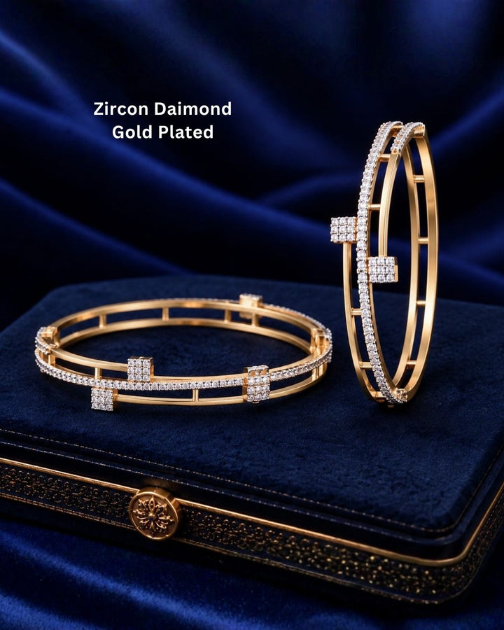 Pair of gold plated crystal bangles displayed on a navy blue jewellery box with a luxurious dark blue background.