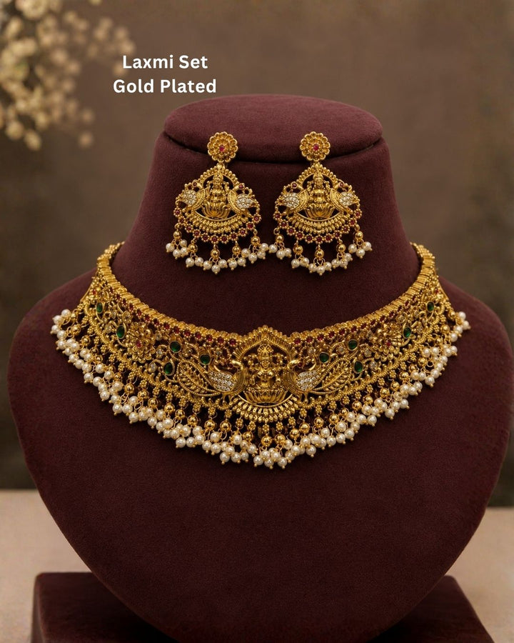 Beautiful temple-style gold plated jewellery set featuring an elaborate necklace adorned with peacock motifs, green and ruby stones, intricate traditional detailing, and cascading pearl drops, paired with matching earrings.