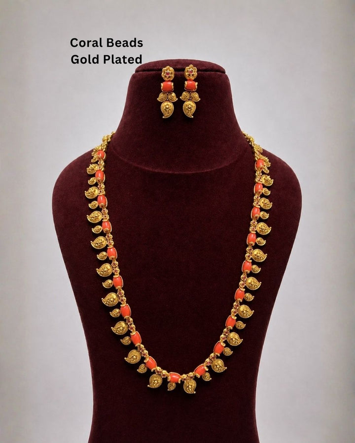 Traditional gold plated long necklace featuring a detailed chain of red beads and intricate gold leaf motifs with dangling coin embellishments. Perfect for weddings, festive occasions, traditional wear, bridal styling, parties, and special occasions.