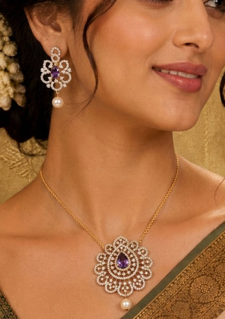 South Indian woman styling a zircon diamond gold plated pendant set with matching earrings. The jewelry features brilliant diamond-look zircon stones, emerald red teardrop stones, intricate floral motifs and elegant pearl drops that beautifully complement sarees, lehengas, gowns and festive ethnic wear for weddings, receptions and special occasions.