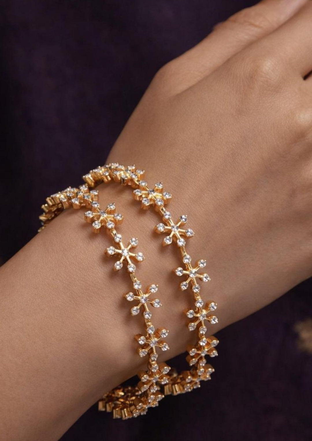 Close-up of a south indian woman wearing Gold Plated Amora Bangles with elegant flower design in star shape and sparkling zircon diamond stones placed in a neat pattern all around the bangles. The bangles give a modern and classy jewelry look with shiny gold finish, lightweight comfort, skin-friendly quality, sweat proof finish, anti-fade colour, and are suitable for functions, parties, festivals, office wear, daily wear and special occasions.