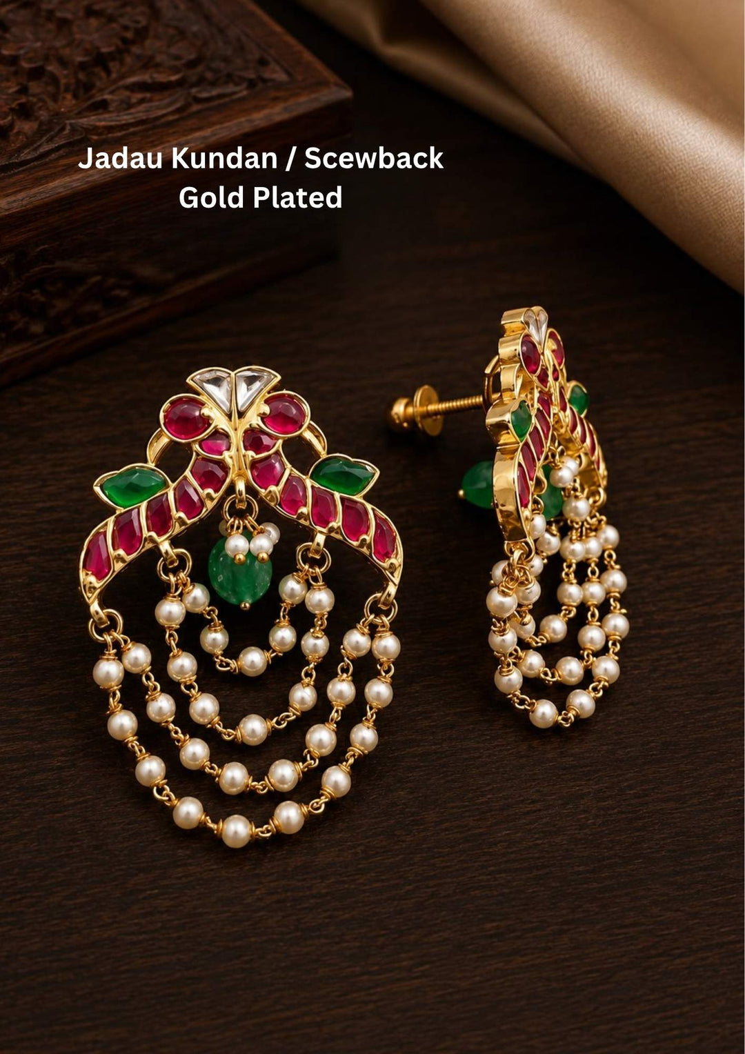 Gold plated Jadau Kundan chandbali style earrings featuring an arched top design decorated with leaf-shaped pink ruby stones, clear kundan inserts, and side accents of green emerald gems. A single smooth green stone drop hangs in the center, while the entire lower frame is adorned with four layered, U-shaped strands of small white pearls attached to delicate gold links, providing a premium heritage appearance suitable for festive wear and traditional occasions.