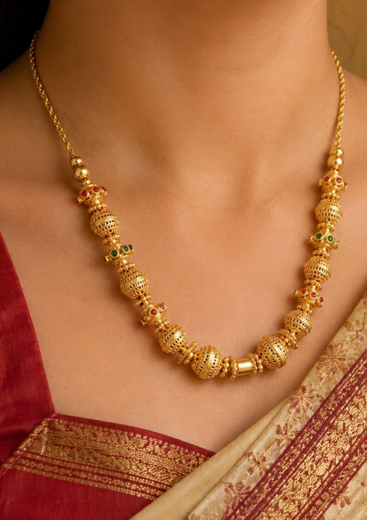 close up of a south indian women neck wearing a Gold plated long chain haraam necklace featuring elegant textured golden spheres alternating with small spacer rings inset with red ruby and green emerald stone accents. This lightweight chain is crafted with a detailed twisted rope style chain extension held in hand to provide a classy and premium appearance suitable for daily wear, office wear, casual outings, family gatherings, festivals, parties and traditional occasions with skin friendly quality, anti fa