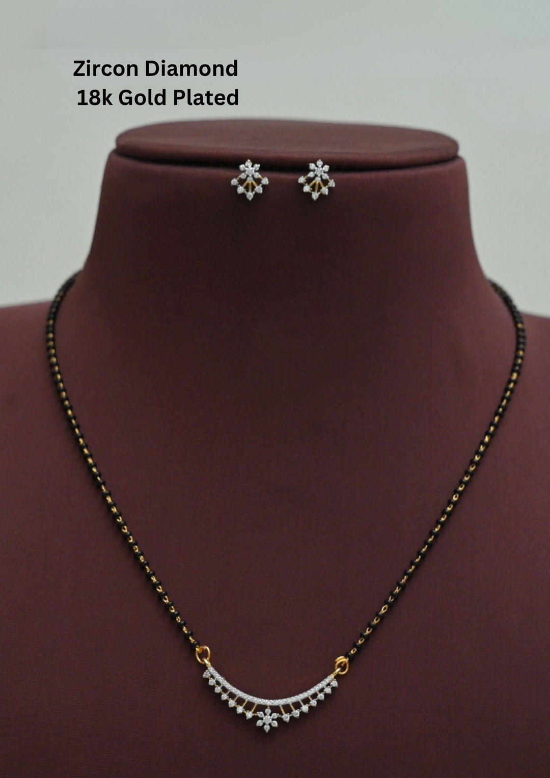 Modern Zircon Diamond gold plated mangalsutra necklace The design features a delicate gold chain transitioning into sections of traditional small black beads on both sides. The central pendant showcases a sleek, contemporary curved Arch with flower pendant with sparkling white cubic zirconia stones. It comes with matching flower studs. This elegant neckpiece perfect for daily wear, office wear, and casual outfits.