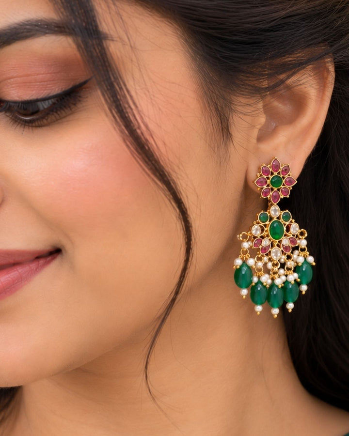 Traditional gold plated designer necklace and earrings set featuring intricate floral motifs with green and ruby-colored stones, sparkling white stones, pearl embellishments, and multiple green bead drops, perfect for festive, wedding, and traditional occasions.