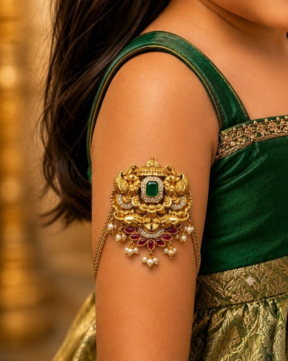Beautiful gold plated kids vanki featuring an intricately crafted traditional design with a large green stone centerpiece, sparkling clear stones, ruby floral motifs, and elegant pearl drops. Perfect for traditional wear, weddings, festivals, classical dance, special occasions, and gifting.