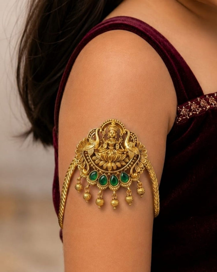 Beautiful gold plated kids vanki featuring an intricately crafted Goddess Lakshmi design with a lotus motif, four green stones, detailed traditional patterns, and elegant dangling gold embellishments. Perfect for traditional wear, weddings, festivals, classical dance, special occasions, and gifting.