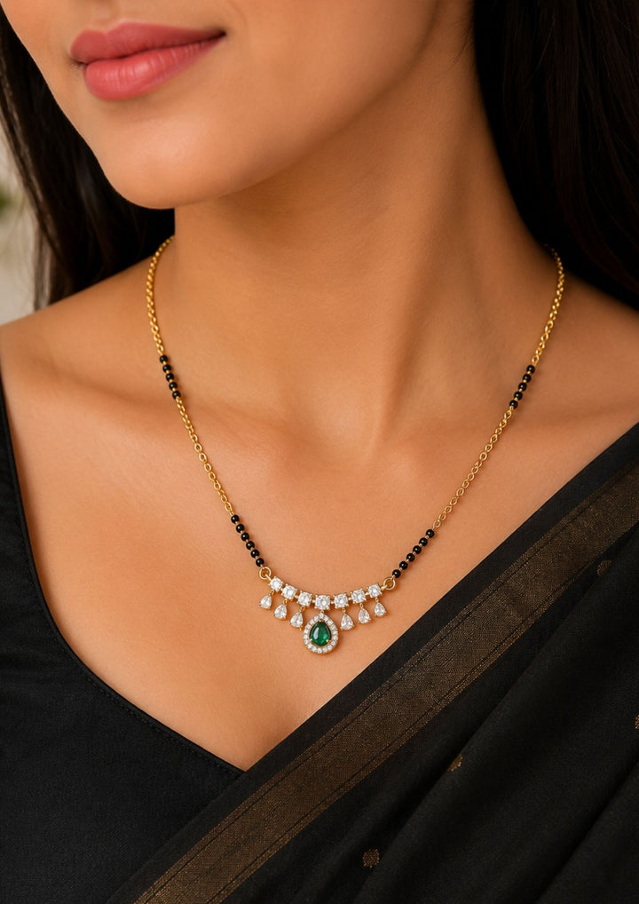 Elegant gold plated black bead mangalsutra showcasing a green gemstone pendant with sparkling zircon detailing and drop charms, perfect for daily wear, office, festive occasions, and traditional styling.