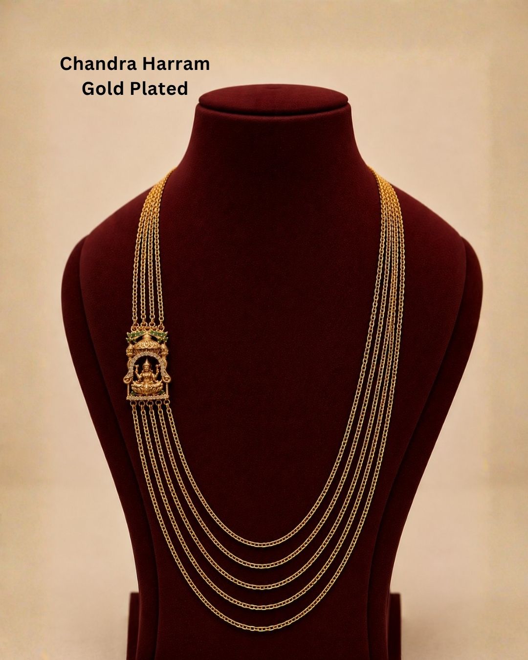 Gold-plated pendant necklace with a decorative floral design and small clear stones, displayed on a dark burgundy background with a gold satin fabric accent. Text overlay reads &
