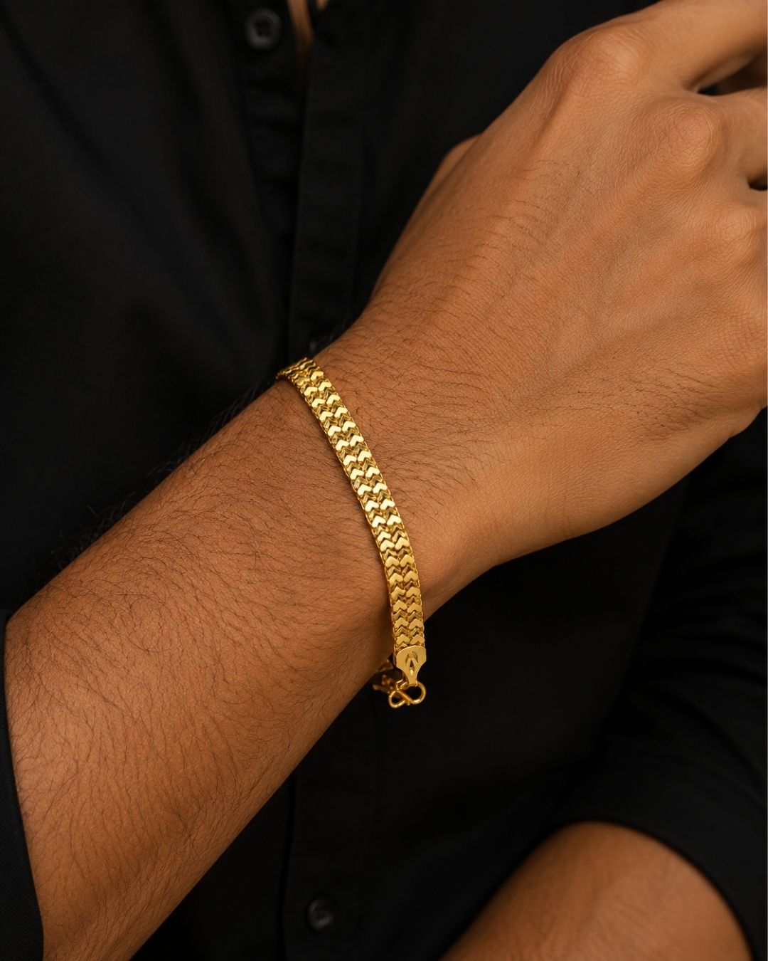 A close-up of a person's wrist wearing a textured gold chain bracelet, paired with a black button-down shirt.