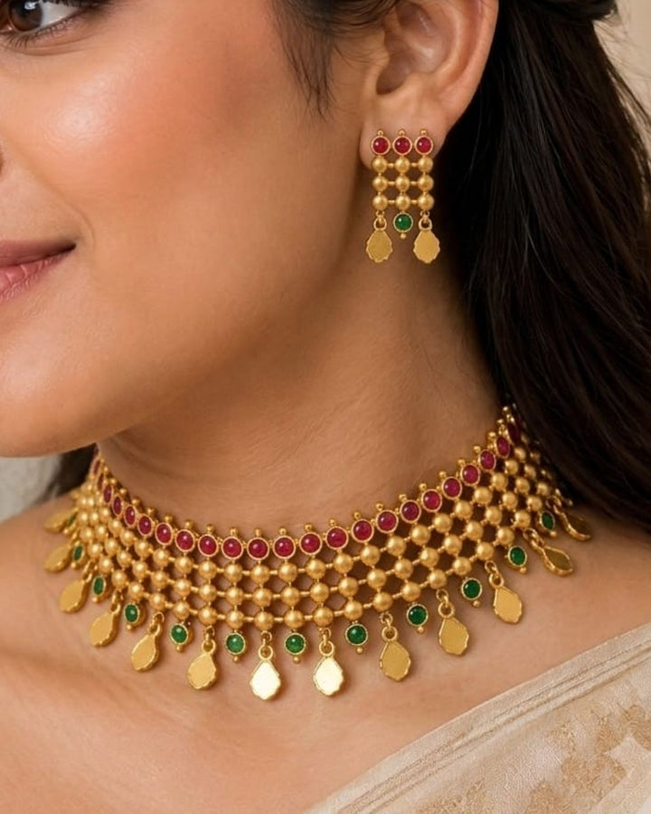 South Indaian women Beautiful Jadau Kundan gold plated necklace set featuring an intricate multi-layered choker design with ruby and green stones, detailed gold beadwork, dangling motifs, and matching earrings. Perfect for festive occasions, traditional wear, weddings, and gifting.