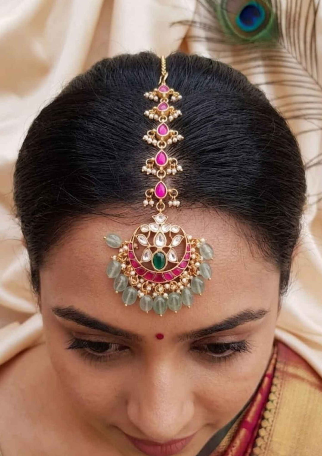 South indian women wearing Gold plated traditional maang tikka hair accessory featuring a beautiful, structured centerpiece intricately set with shimmering white Jadau Kundan stones in a classic floral or geometric layout. The main pendant is designed to rest elegantly on the forehead, connected to a polished gold link chain, and is finished with a delicate row of hanging white pearl drops at the bottom for a timeless, regal look.