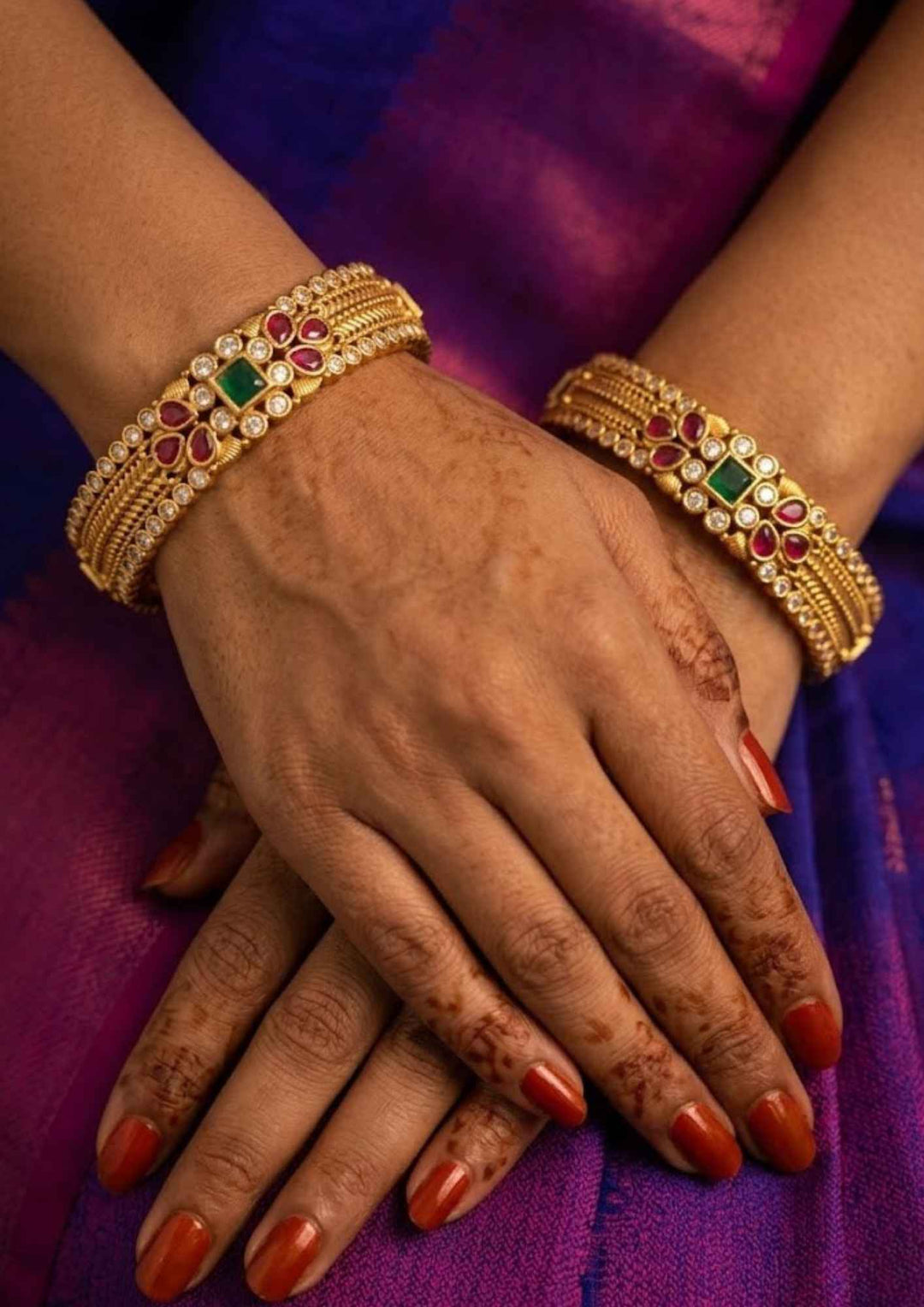 close-up of a South Indian women wearing Jadau Kundan Gold plated Bangles (set of 2) design with Ruby and emerald gold plated kemp with rows of square-cut red kempu stones, tiny white crystal borders, and holding a green emerald stone. They have a premium gold finish, are lightweight, and comfortable to wear. Suitable for daily wear, pooja, weddings, festivals, functions
