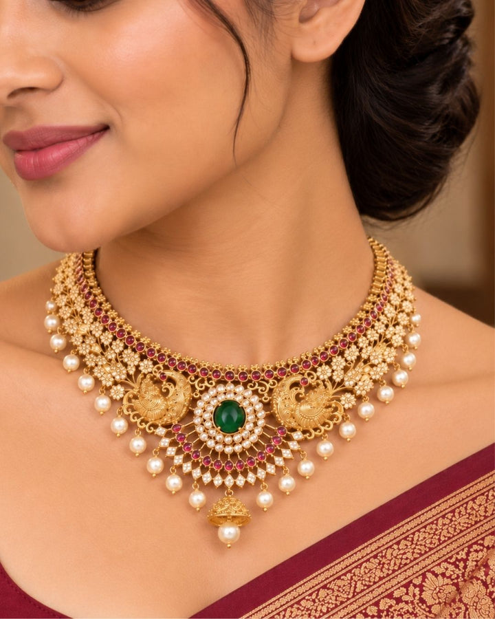Gold pleted jadau kundan chocker set designed with twin peackocks and in center big emerald stone and bottom comes with bell and pearls to entire chocker and this set comes with matching big earrings perfect for birdal wear, functions
