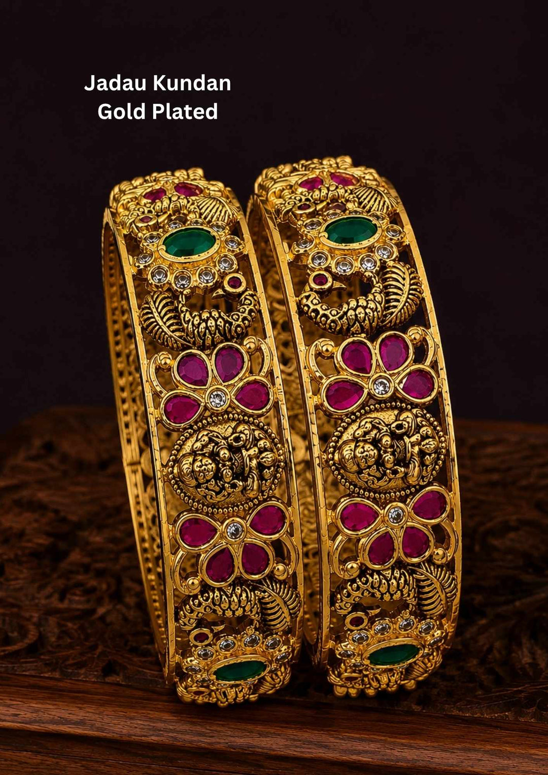 A pair of thick Jadau Kundan gold-plated kada bangles featuring intricate traditional motifs. The design showcases detailed peacock carvings, floral patterns inset with ruby-pink and emerald-green stones, and delicate white Kundan accents running along an antique gold-finished frame. perfect for weddings and festive wear.