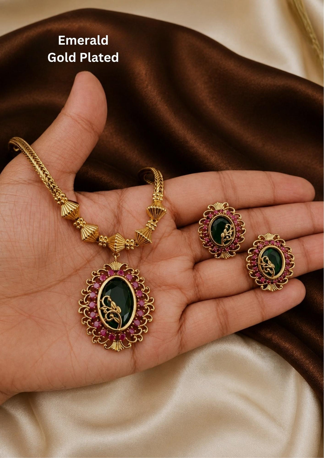 Jadau Kundan Gold Plated Rudy pendant necklace and matching stud earrings set. The necklace features a smooth gold chain with small bead dark green stone pendant surrounded by a border of tiny pink ruby stones. This elegant, lightweight set is perfect for office wear, kitty parties, and daily use.