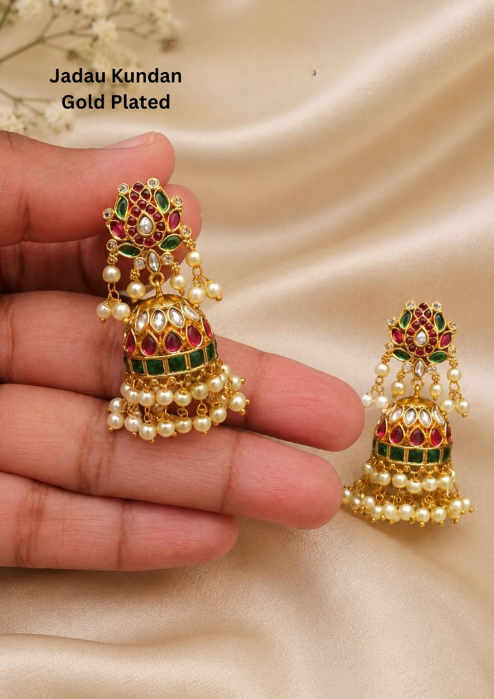 Jadau Kundan Jhumka Earrings with traditional floral design, red ruby stones, green stone detailing, and with beautiful guttapusalu hanging pattern, and old age buttalu style. The earrings have a rich bridal jewelry look with shiny gold finish, lightweight feel, sweat proof quality, anti-fade colour, and are perfect for weddings, festivals, functions, and traditional wear.