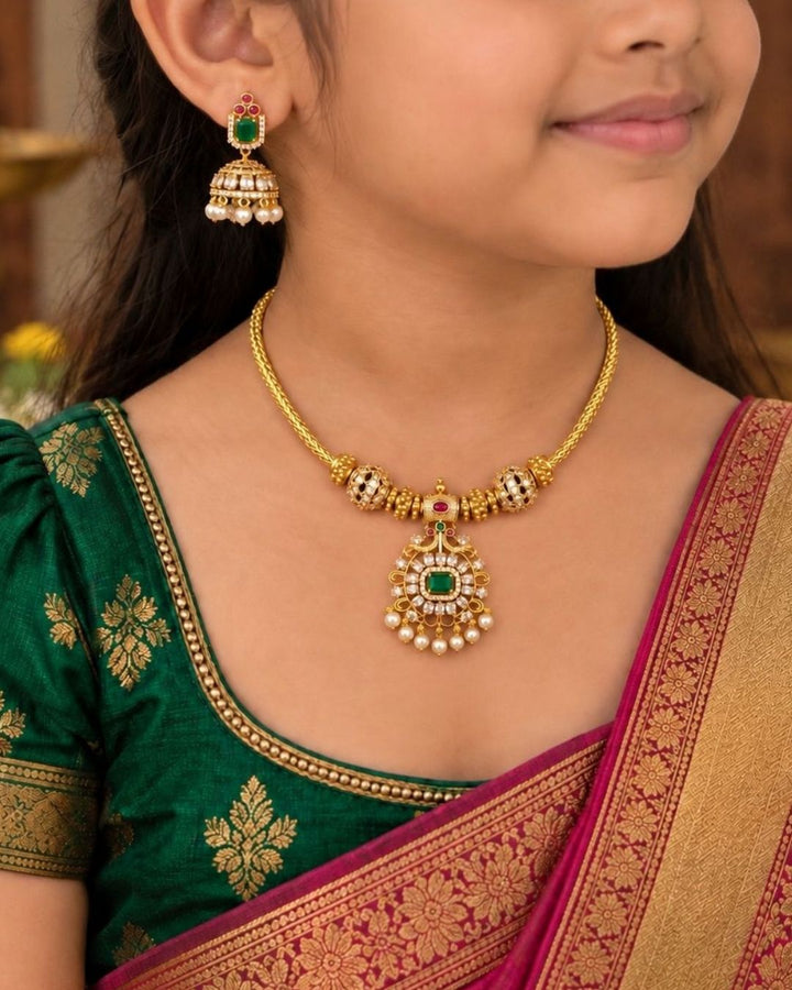 gold plated Jadau Kundan jewelry set with a sleek gold chain attached to structured gold beads. It centers a grand round medallion pendant encrusted with glittering white kundan stones, with emerald-green center stone, dual gold peacock motifs at the top, and white pearl drops at the bottom. Includes a matching pair of elegant hanging jhumka earrings Perfect for festive occasions with skin-friendly premium quality