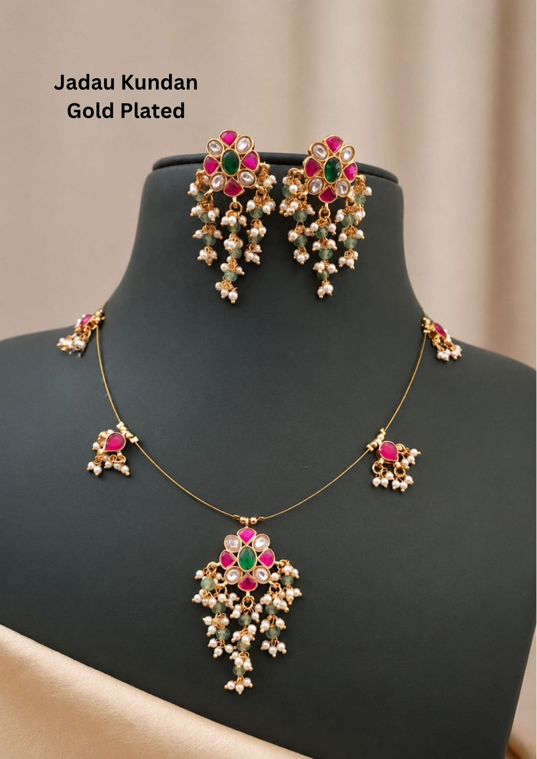 Traditional Jadau Kundan gold plated necklace and matching earrings set. The sleek chain necklace features a central floral pendant set with a green emerald center, ruby pink stones, and white kundan details, finished with guttapusalu of small green beads and white pearls. Matching small charms dangle along the delicate gold wire chain. Perfect for weddingwear, festivals and it is anti fade color.
