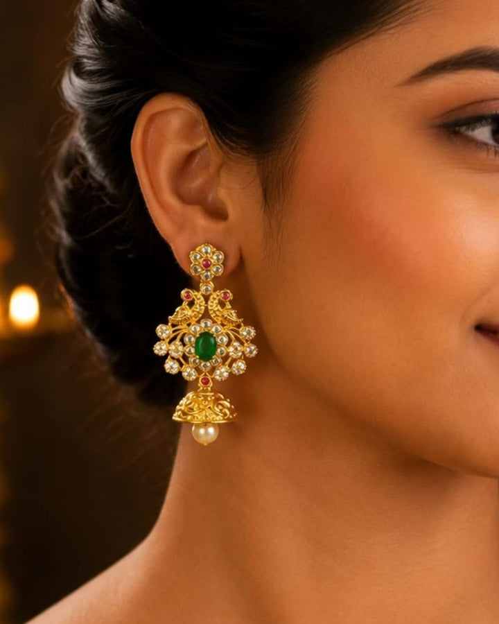 Beautiful green stone gold plated jhumka earrings featuring peacock-inspired detailing, colorful stone accents, and pearl drops. Perfect for festive occasions, traditional outfits, parties, and gifting.