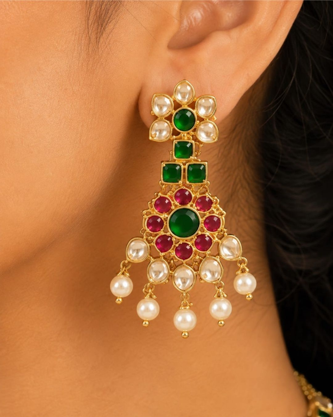 A south indian woman wearing an ornate gold-toned traditional jewelry set with deep red stones, including a necklace, matching earrings, and a forehead ornament, paired with a navy blue embroidered saree.