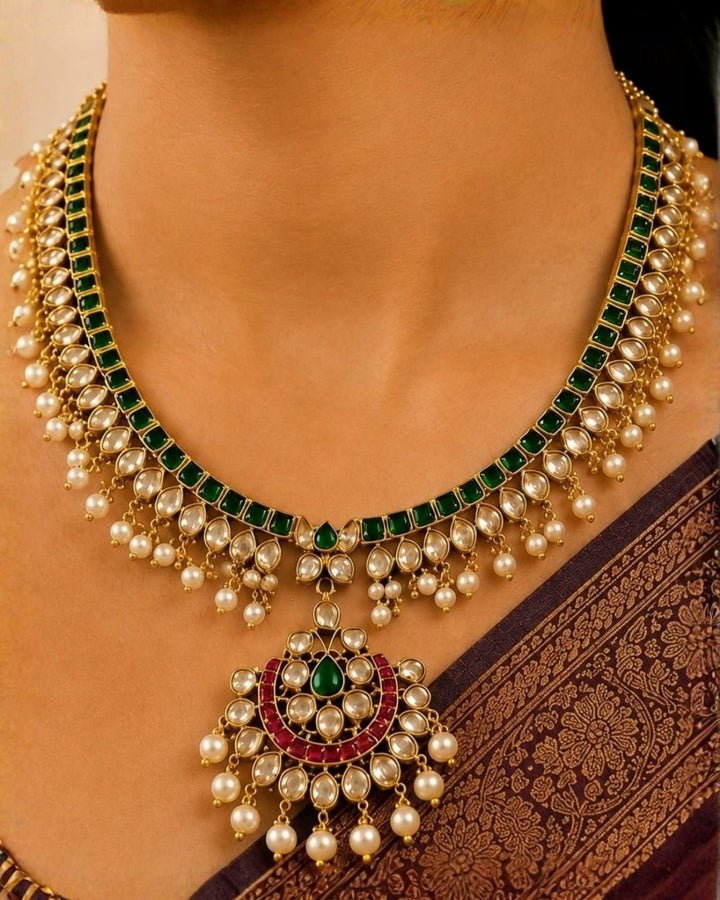 A south indian woman wearing an ornate gold-toned traditional jewelry set with deep red stones, including a necklace, matching earrings, and a forehead ornament, paired with a navy blue embroidered saree.
