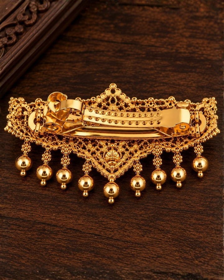 Laxmi gold plated hair clip designed with goddess Lakshmi in antique temple jewelry design, shining with white stones and hanging gold bead drops, with metal clip closure, suitable for bridal hairstyles, weddings, festivals, poojas, Bharatanatyam, sarees, lehengas, and traditional South Indian ethnic hair styling with rich royal appearance.