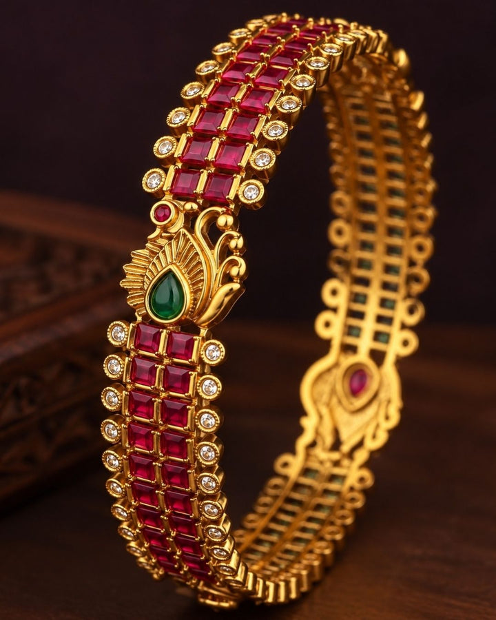 Premium gold-plated real Kemp peacock bangles designed with multiple rows of square-cut red Kemp stones, with white crystal borders, and an ornate golden peacock design centered with a water drop green stone. It is lightweight, skin-friendly, and anti-fade bangles are perfect for poojas, festive wear, and dailywear.