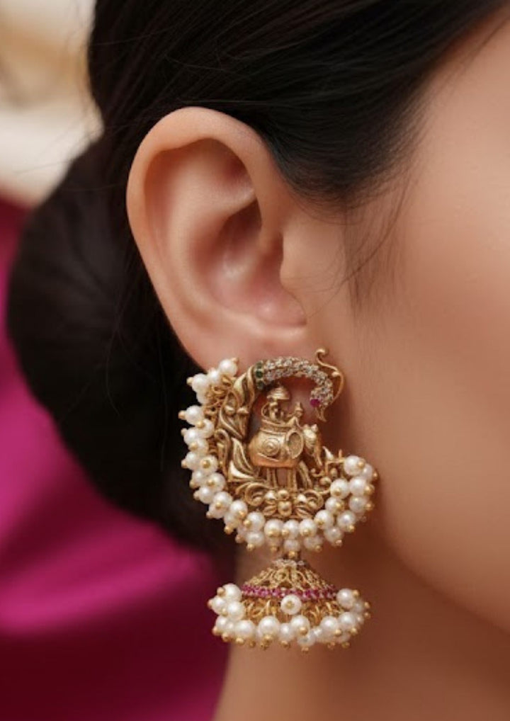 closse up of a women wearing a Traditional style gold plated Guttapusalu jhumki earrings designed with detailed elephant and peacock structures, pink stone accents, and bunch clusters of hanging white pearls that give a graceful traditional look for festive celebrations, poojas, family functions, and bridal outfits with lightweight comfortable use