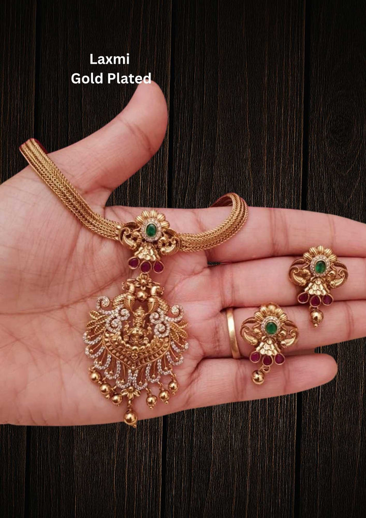 Gold-plated necklace and earrings set and in image clearly shown how it looks matching earrings, green stones, zircon detailing, and pearl drops. The temple jewelry design features Goddess Laxmi pendant with floral traditional patterns and antique gold finish. The layered necklace and matching earrings give a grand and elegant ethnic jewelry appearance. Comfortable, skin-friendly, sweat proof, and perfect for weddings, festivals, sarees, and family functions.