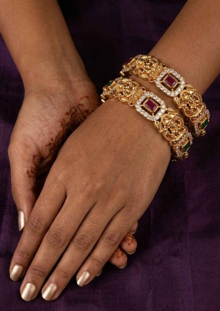 South Indain Women wearing a 
gold plated nakshi frame Goddess Lakshmi temple bangles showing alternating ruby and emerald stone inserts that give a graceful traditional and modern look for marriage functions with COD.