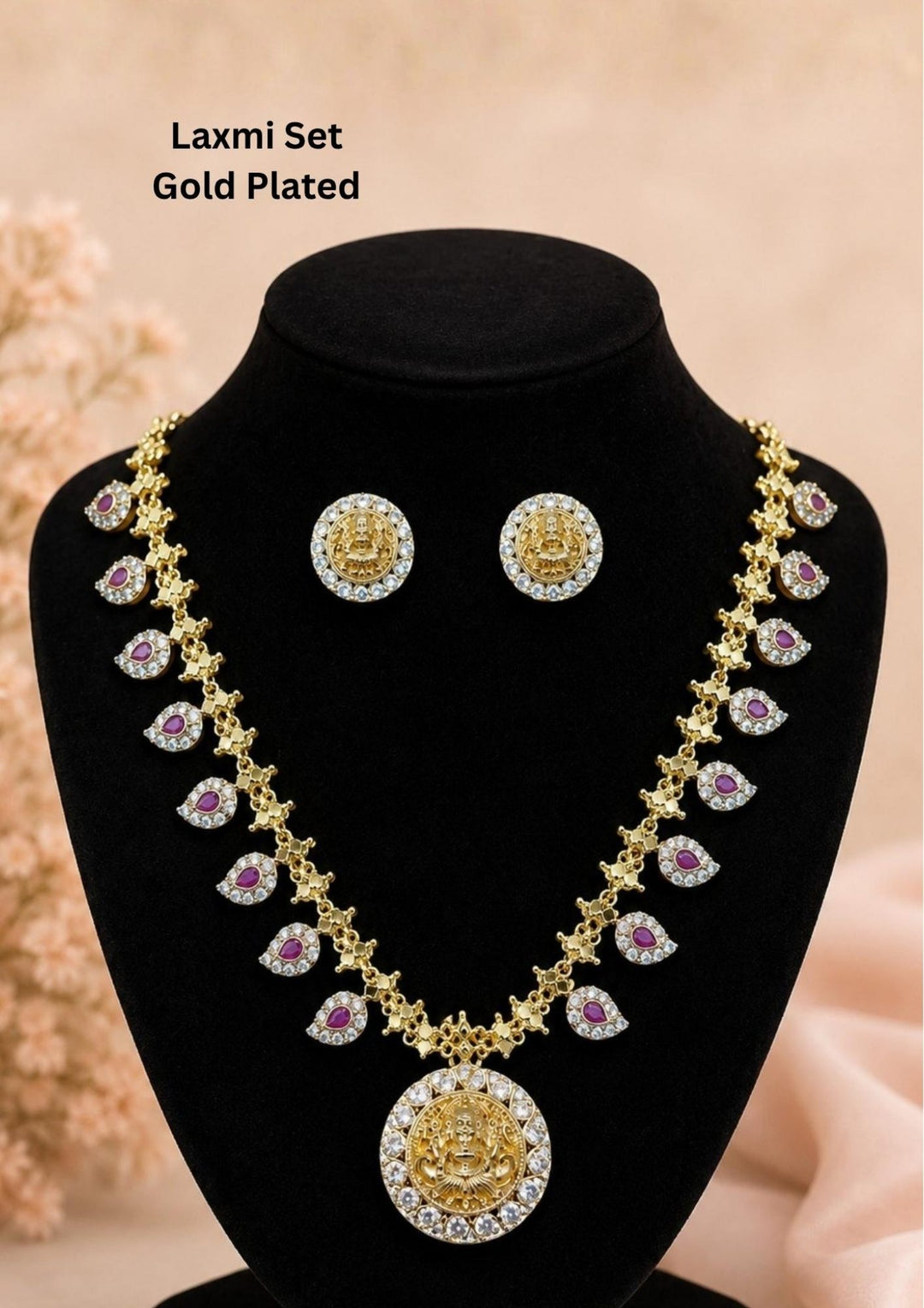 Elegant gold plated Lakshmi necklace set featuring ruby teardrop stones, sparkling zircon detailing, and a beautifully crafted Goddess Lakshmi pendant with matching designer stud earrings. Perfect for festive and bridal wear.