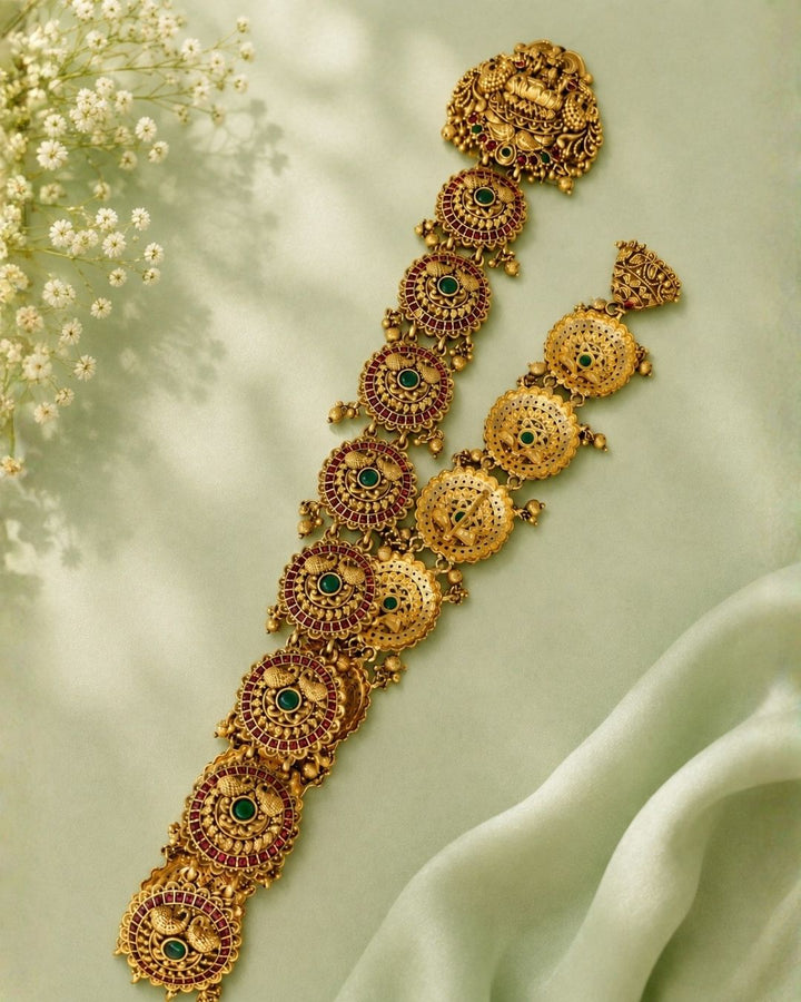 Gold-toned traditional Indian jewelry set featuring a necklace and matching earrings displayed on a black jewelry bust against a dark purple background.