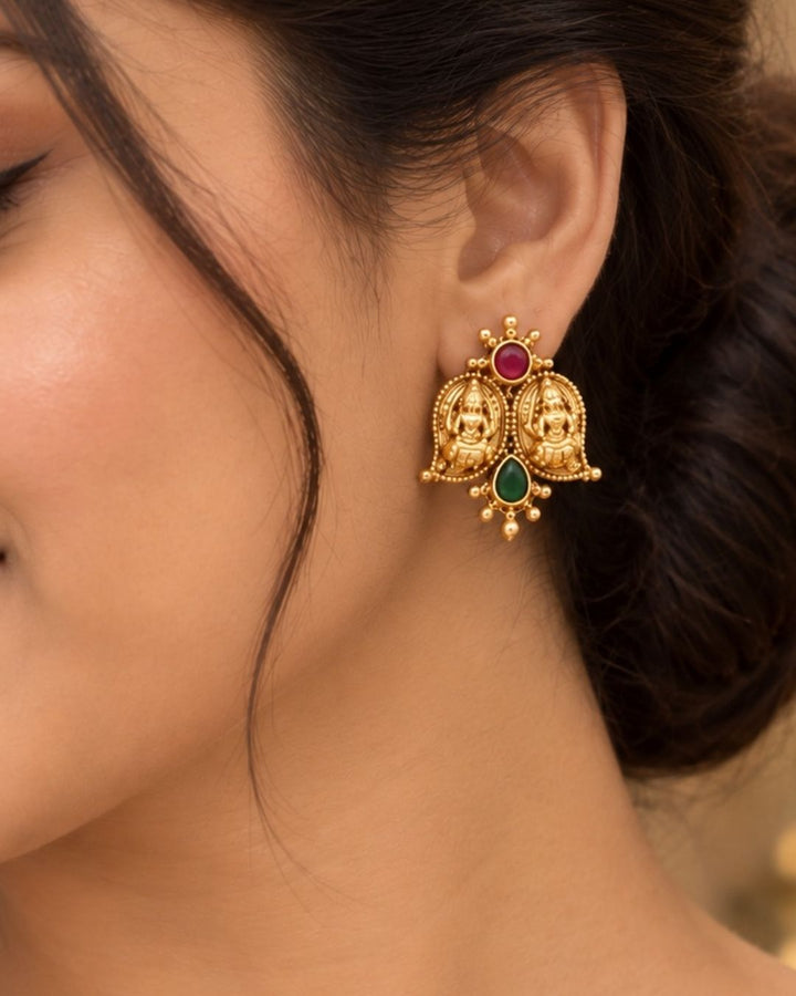 Elegant gold plated Lakshmi Devi necklace set featuring multiple detailed temple motifs, red and green stone embellishments, a central green teardrop pendant, and matching earrings, perfect for festive and traditional occasions.