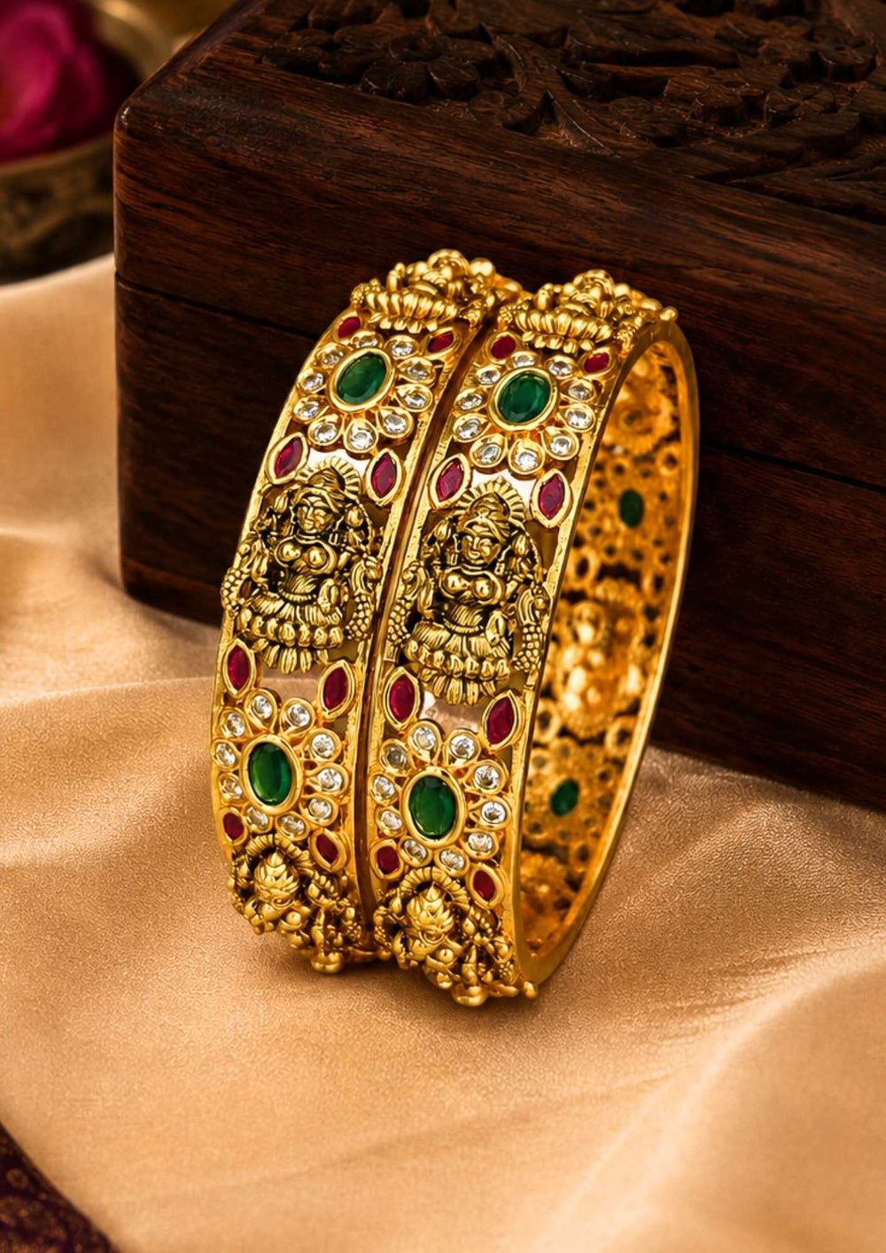 Pair of gold bangles with gemstones on a beige fabric background