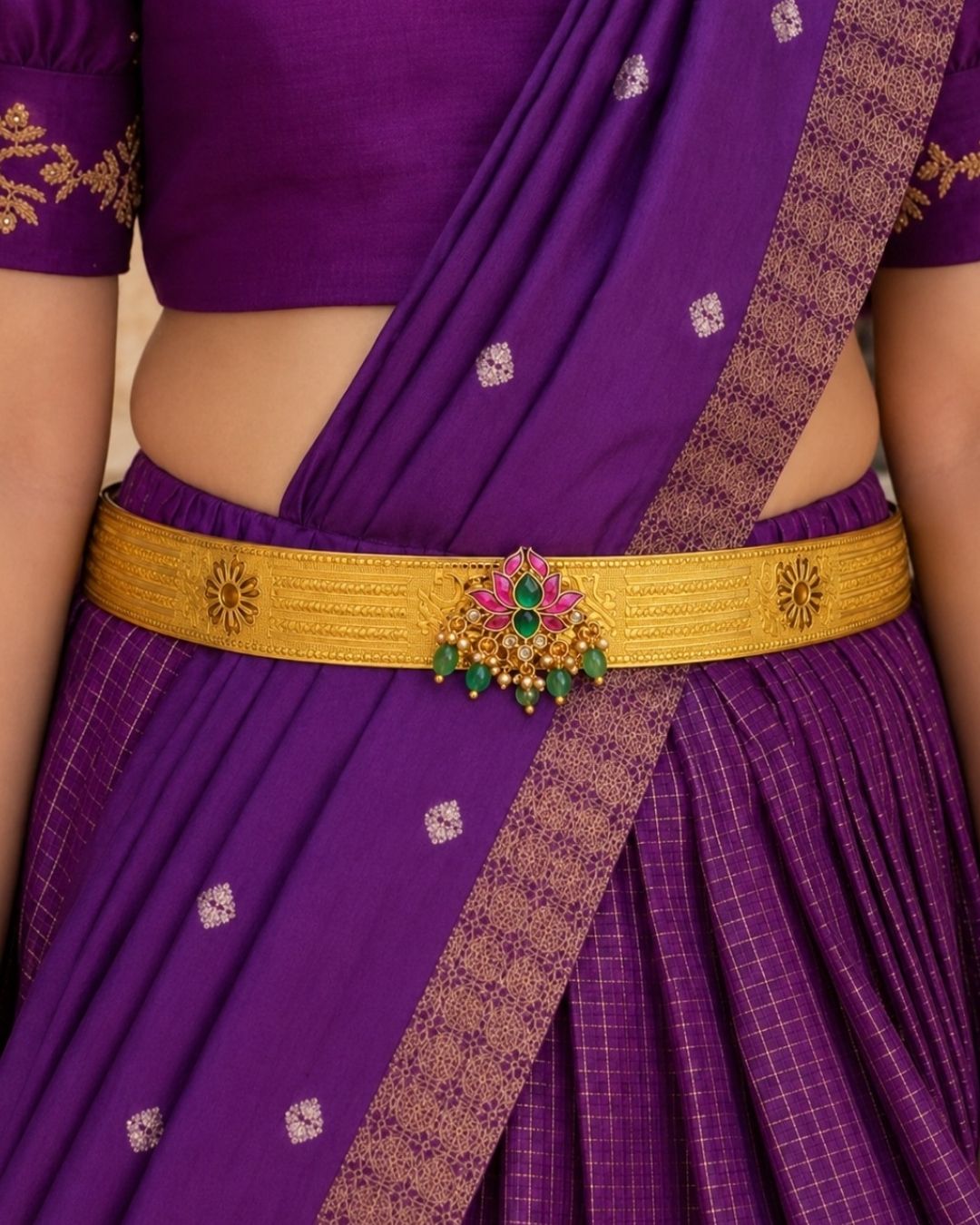 Beautiful gold plated kids hip belt featuring a wide intricately engraved band with traditional floral motifs and a decorative centerpiece adorned with vibrant green and pink stones, sparkling clear stones, and elegant green bead drops. Perfect for traditional wear, weddings, festivals, classical dance, special occasions, and gifting.