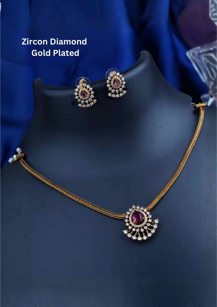 A minimalist 18k gold plated herringbone chain necklace featuring a central teardrop-shaped ruby pink stone. The stone is enclosed in a halo of white pure Zircon diamonds that flares out at the bottom into a shimmering, fan-shaped scalloped fringe, paired with matching crown-set ear studs.