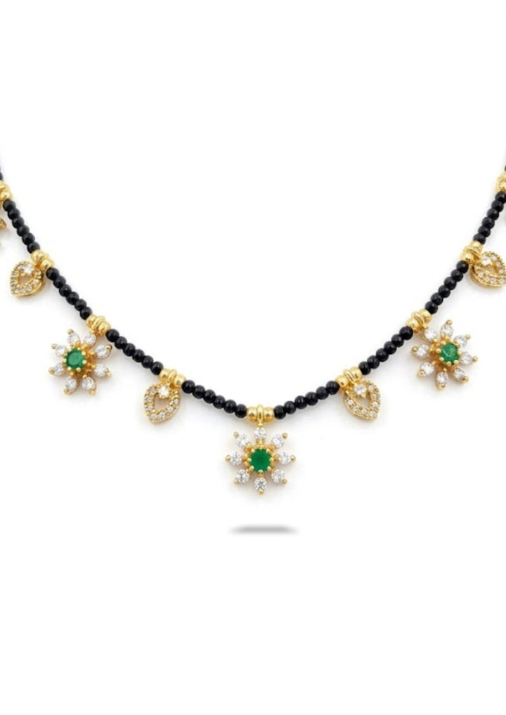Necklace with black beads and gold and green floral pendants on a white background
